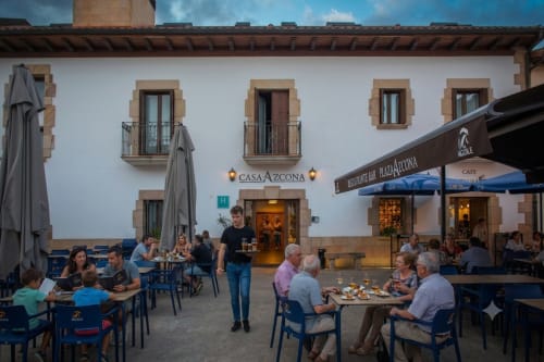 Terrasse de la cour Casa Azcona à Zizur Mayor avec clients aux tables extérieures et façade blanche