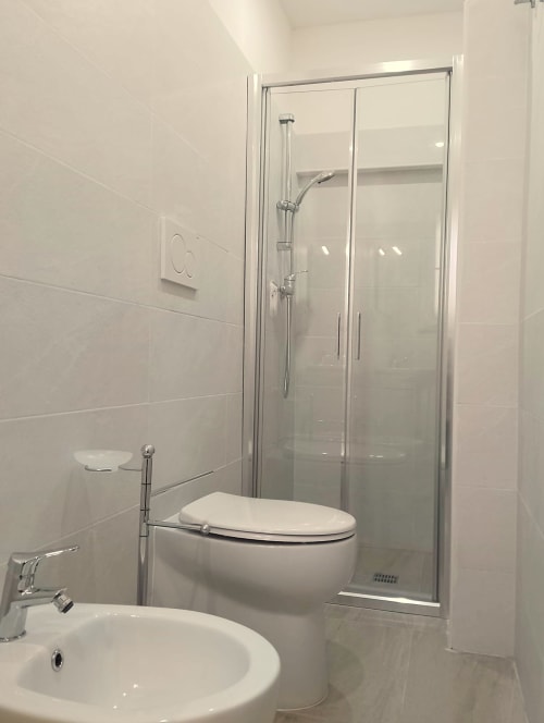 Bagno moderno della Guest House Il Corso a Veglie con piastrelle bianche, cabina doccia in vetro, wc e lavabo rotondo