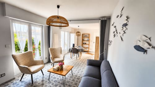 Salon moderne de la villa Ô de Mer à Sangatte avec fauteuils à motifs, canapé gris, accents bois et vue sur le jardin