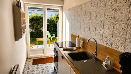 Cuisine moderne avec vue sur le jardin de la villa Maison Ô de Caps à Sangatte, comptoirs en bois et dosseret à motifs.