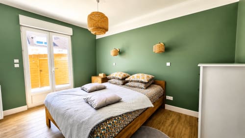 Chambre de la villa Ô de Mer à Sangatte avec murs verts, lit en bois, luminaires suspendus tissés et portes donnant sur le jardin