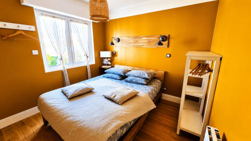 Chambre jaune éclatante à la villa Ô de Mer près de la plage de Sangatte, avec lit queen-size aux oreillers bleus et mobilier moderne