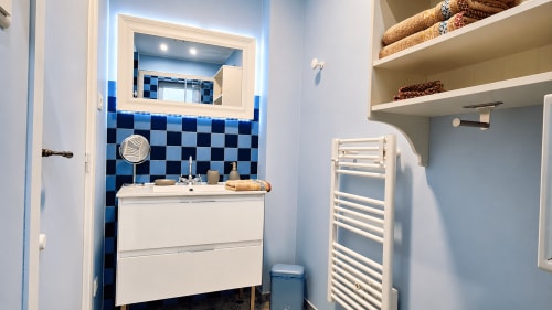 Salle de bains moderne de la villa Ô de Mer à Sangatte avec carrelage bleu à carreaux, vasque blanche et sèche-serviettes électrique