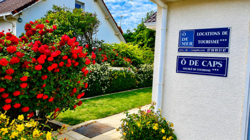 Entrée du jardin de la villa Ô de Caps à Sangatte avec roses rouges, fleurs jaunes et panneaux touristiques bleus