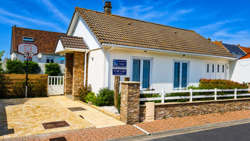 Villa Ô de Caps à Sangatte : façade blanche, toiture carrelée, volets bleus, allée en briques, clôture blanche près de la plage