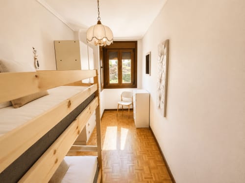 Dormitorio minimalista y luminoso en el albergue Holibai de Baiona con camas de madera, luz colgante y puertas de madera.