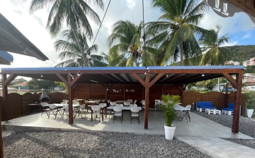 Espace de réception en plein air aux Créolines avec pergola en bois, tables de repas, palmiers et vue sur le jardin