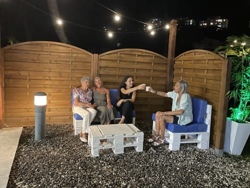 Quatre femmes discutent dans la salle de réception de groupe des Créolines, avec des paravents en bois, des guirlandes lumineuses et vue sur le jardin