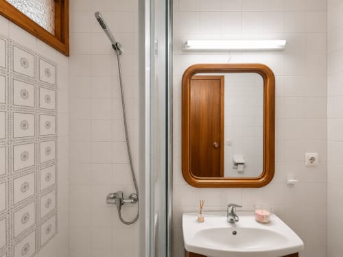 Baño moderno en apartamento Holibai, Baiona con espejo de marco de madera, lavabo blanco y ducha tipo lluvia