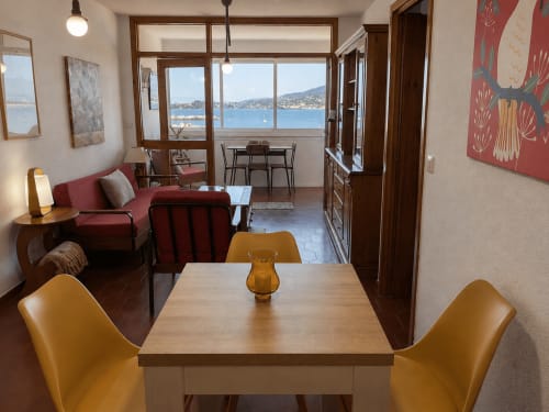 Apartamento moderno en Baiona con vistas al mar, mesa de comedor, sofá rojo y ventanales que dan a la costa