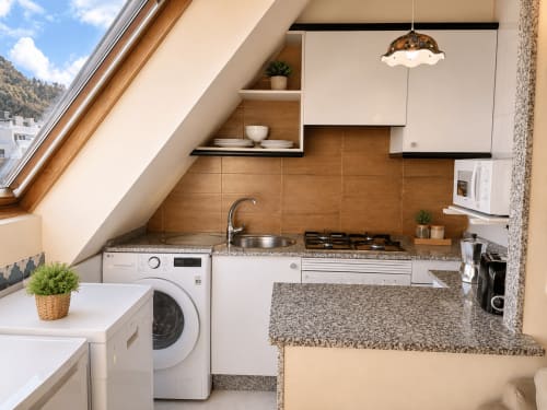 Cocina moderna en buhardilla de Baiona con techo abuhardillado, electrodomésticos blancos, revestimiento de madera, encimeras de granito y vistas a la ciudad