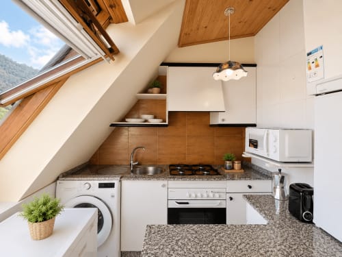 Cocina moderna en ático de apartamento en Baiona con electrodomésticos de acero inoxidable, encimeras de granito y detalles de techo de madera