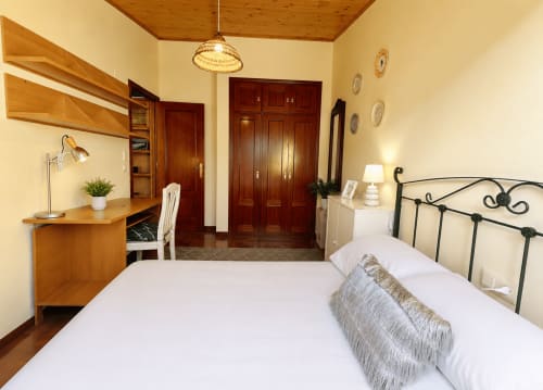 Dormitorio luminoso del apartamento Holibai en Baiona con cama blanca, escritorio de madera y vistas a la ciudad
