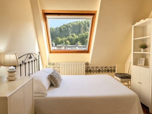 Dormitorio luminoso en buhardilla de Baiona con claraboyas, vistas al bosque, cama de hierro forjado y decoración blanca