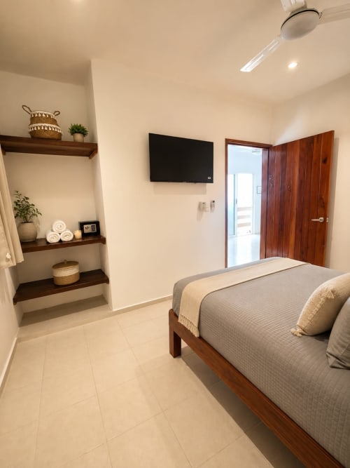 Moderna habitación del Hotel Isla Mujeres Centro con cama de madera, TV mural, estanterías integradas y puerta de madera hacia