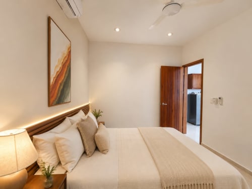 Habitación moderna en Hotel Isla Mujeres Centro con cama de madera, ropa blanca, iluminación cálida y puerta de madera hacia baño privado