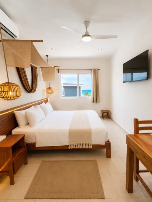 Suite luminosa en Hotel Isla Mujeres Centro con cama de madera, vista al océano, ventilador de techo y decoración costera
