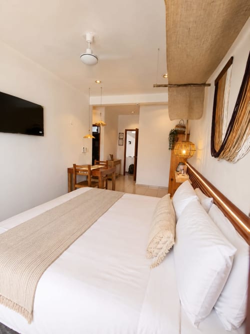 Habitación luminosa en Hotel Isla Mujeres Centro con cama queen, muebles de madera, lámparas colgantes y plano abierto hacia comedor