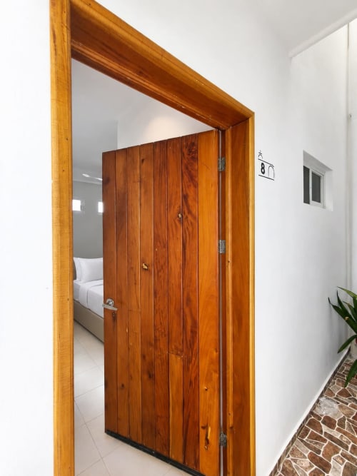 Puerta de madera de entrada a la Suite 8 del Hotel Isla Mujeres Centro, mostrando dormitorio con ropa de cama blanca