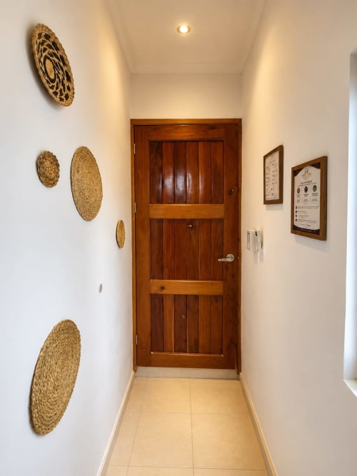 Entrada del pasillo en Hotel Isla Mujeres Centro con puerta de madera, decoraciones tejidas en la pared y cuadros enmarcados