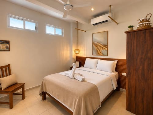 Dormitorio moderno en Hotel Isla Mujeres Centro con cama de madera, ropa de cama blanca, aire acondicionado, iluminación colgante y ambiente cálido