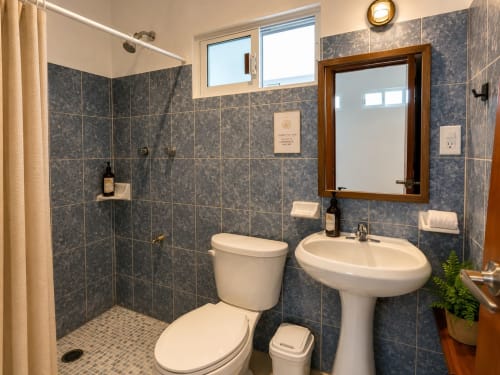 Baño moderno en Suite 8 del Hotel Isla Mujeres Centro con lavamanos de pedestal, inodoro y ducha a ras de suelo con azulejos azules