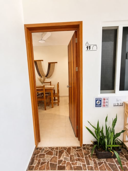Entrada de la Suite 11 en Hotel Isla Mujeres Centro con puerta de madera, piso de azulejos y habitación amueblada visible