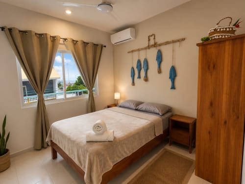 Habitación de hotel luminosa en Isla Mujeres Centro con cama de madera, vistas al océano, decoración de peces azules y armario de madera.
