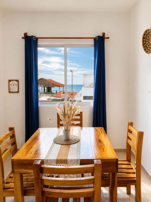 Comedor del hotel en Isla Mujeres con mesa de madera, cortinas azules y vista al océano a través de ventanal