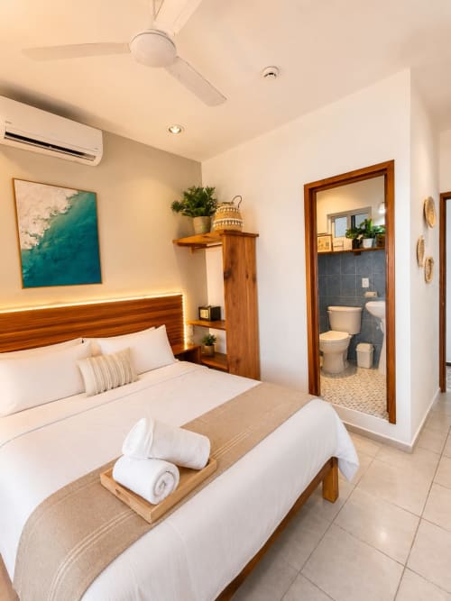 Suite de hotel en Isla Mujeres con cama de cabecera de madera, baño privado, arte oceánico turquesa y comodidades modernas