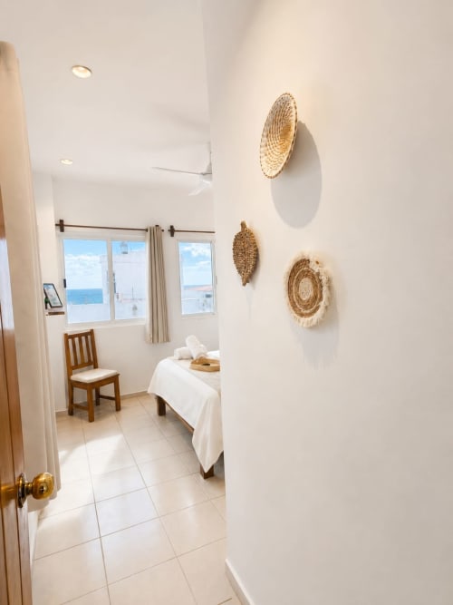 Luminosa habitación de hotel costero con vistas al mar, decoración tejida en paredes, cama blanca y silla de madera en Hotel Isla Mujeres Centro
