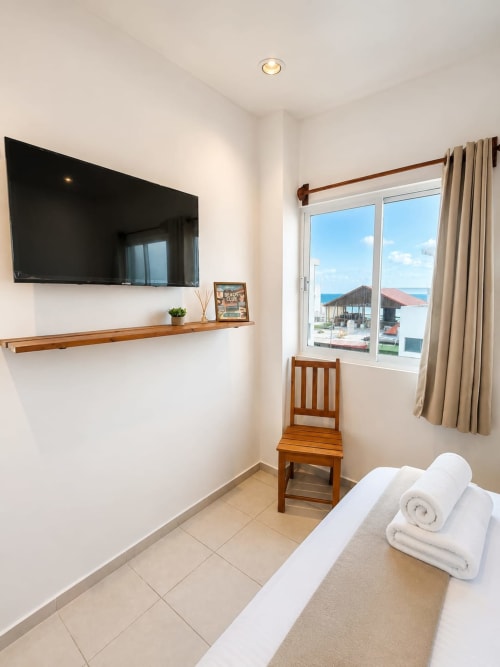 Habitación moderna en Hotel Isla Mujeres Centro con TV de pantalla plana, silla de madera, toallas blancas y vistas al océano