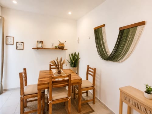Área de comedor del Hotel Isla Mujeres Centro con mesa de madera, sillas y hamaca rayada verde sobre paredes blancas