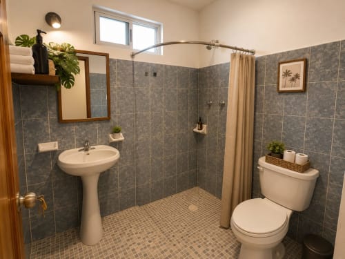 Baño moderno en suite del Hotel Isla Mujeres Centro con ducha amplia, lavamanos pedestal, inodoro y piso de cerámica.