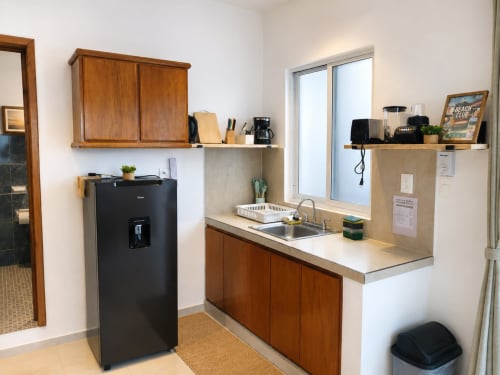 Pequeña cocineta en suite de hotel en Isla Mujeres con refrigerador negro, fregadero, gabinetes de madera y acero inoxidable