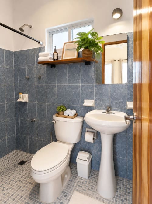 Baño moderno del Hotel Isla Mujeres Centro con lavamanos pedestal, inodoro, azulejos azules y espejo con marco de madera
