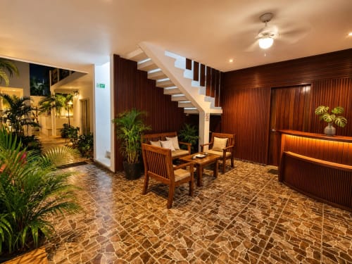 Vestíbulo del Hotel Isla Mujeres Centro con escaleras de madera, zona de descanso, plantas tropicales y piso de ladrillo.