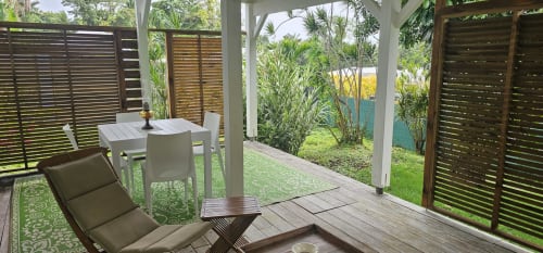 Terrasse ombragée de l'Habitation Villa Les Cassias à Petit-Bourg, avec chaise longue, table de repas et vue sur un jardin luxuriant