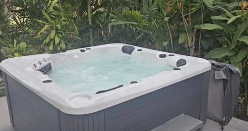 Baignoire spa extérieure aux eaux turquoise avec jets noirs, entourée de luxuriantes plantes tropicales à l'Habitation Villa Les Cassias
