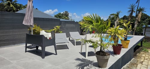 Moderne Terrasse der Villa Les Cassias mit Liegestühlen, Topfpflanzen, Poolblick und dunklem Gebäude in Petit Bourg