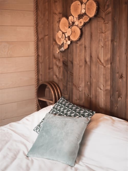 Cozy bedroom at Les Murmures du Bois with patterned pillows on white bedding, wooden headboard, and rustic wood walls in