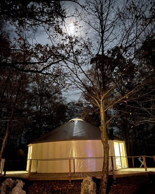 Illuminated yurt cabin nestled in forest at Les Murmures du Bois, Sousceyrac-en-Quercy, with warm interior glow and bare