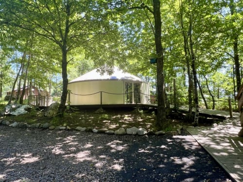 Glamping tent nestled in forest at Les Murmures du Bois, Sousceyrac-en-Quercy, with wooden deck and lush tree canopy