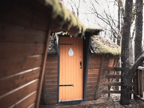 Orange wooden guest cabin with moss-covered roof at Les Murmures du Bois forest BnB in France