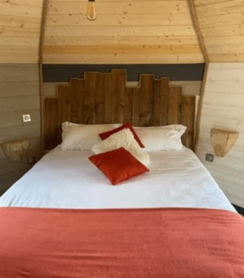 Chambre accueillante aux Murmures du Bois : tête de lit en bois, literie blanche, touches rouges et vue sur le jardin