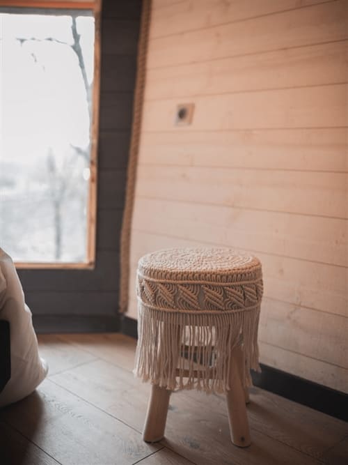 Petit tabouret tressé à franges dans une chambre de charme à Les Murmures du Bois, gîte français