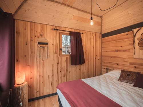 Cozy wooden cabin bedroom at Les Murmures du Bois with bed, warm lighting, and rustic pine interior