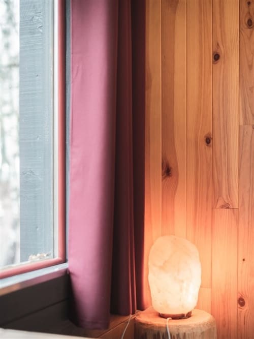 Glowing salt lamp on wooden floor beside window with pink curtain in Les Murmures du Bois bedroom