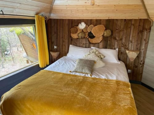 Chambre cosy aux Murmures du Bois avec literie moutarde, murs boisés, vue sur jardin et décoration murale rustique