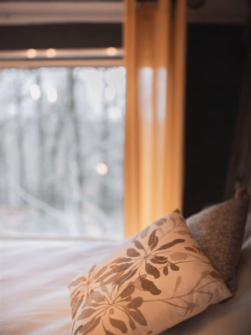 Oreiller décoratif à motif floral sur lit avec vue sur le jardin enneigé des Murmures du Bois